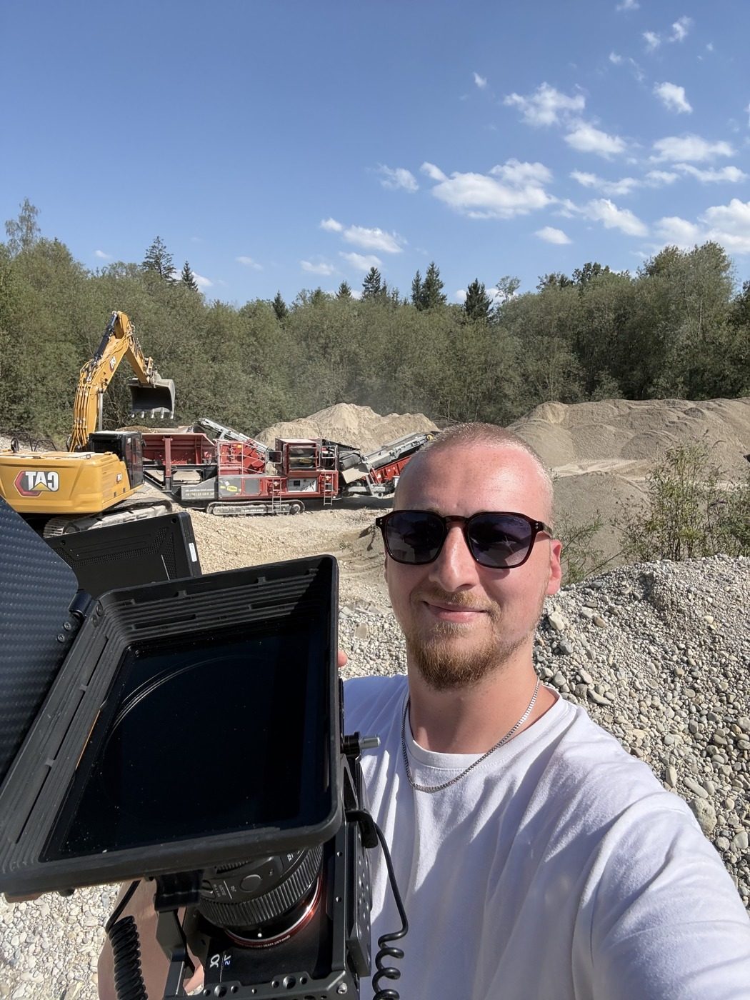 Mario Kaiser mit Kamera und Field-Monitor vor Bagger und Kieshaufen